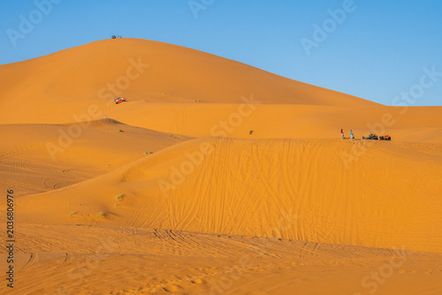Off-road adventure vehicles and tourists exploring golden Sahara dunes near Merzouga, Morocco