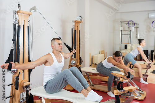 Fotografía Active young man doing arm exercises on cable training device in well-equipped g