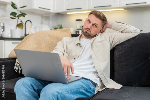 Foto Young man at home works on laptop feels tired and demotivated and takes deep sigh during hard task