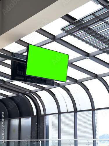 Mockup green screen on a suspended TV monitor in a modern glass airport terminal or public building