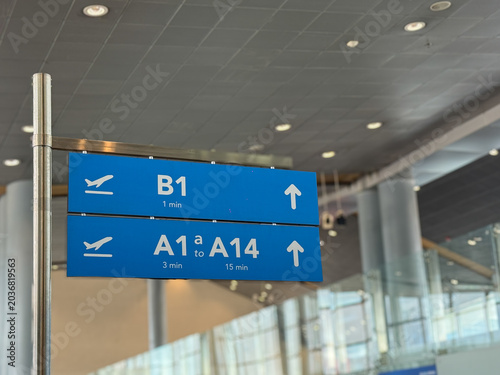 Blue directional sign in a modern airport terminal pointing to boarding gates with walking times