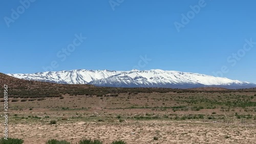 Snow-capped Atlas Mountains rising above arid Moroccan landscape under blue sky