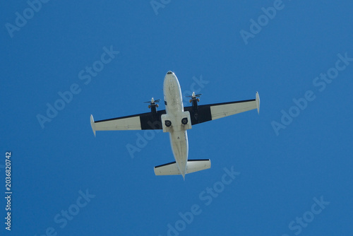 Canvas Print Low Angle View of a Twin-Engine Propeller Plane Flying in Clear Blue Sky on Sunn
