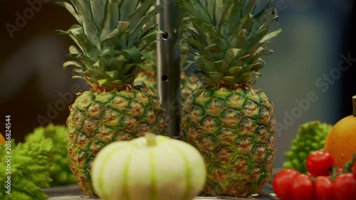A rotating circular platform displaying a carefully arranged assortment of fresh fruits and vegetables. Pineapple placed at the center, surrounded by tomatoes, leafy lettuce bundles, and small pumpkin