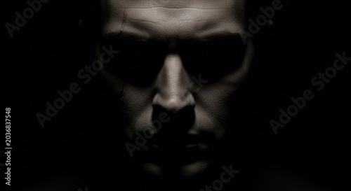 Dramatic close up of a human face with sunglasses in shadow
