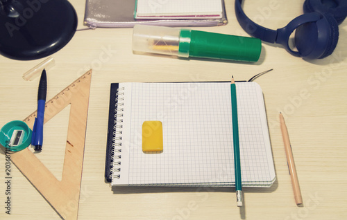 School desk with pens. Black spiral notebook with empty sheet and pencil, eraser, ruler, sharpener, pencil case indoors on a table. Education, business, job, study, back to school idea concept
