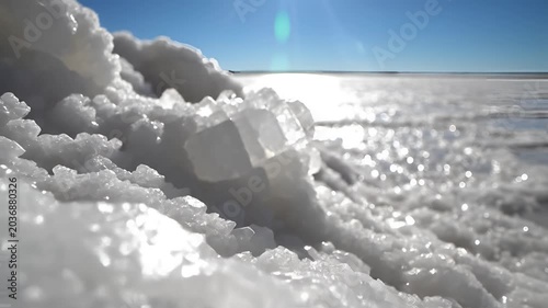 Closeup of sparkling salt crystals on a vast salt flat under a bright blue sky.