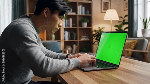 Young Man Typing on Laptop with Green Screen in Cozy Home Office.