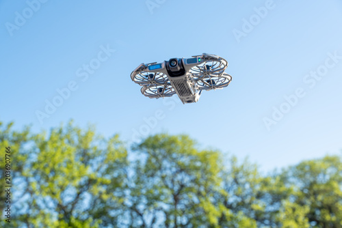 Photography A drone hovering mid-air against a clear blue sky, equipped with a forward-facin
