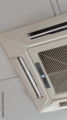 Ceiling cassette air conditioner unit mounted in suspended office ceiling grid, white grille and vents, closeup inspection