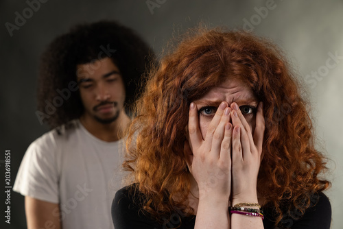 Fotografía Woman feeling fear and stress covering her face with hands as man stands behind