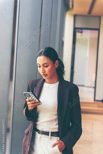 Businesswoman dressed the phone to ear, talking to friend, smiles surprised face in front of a modern glass office building