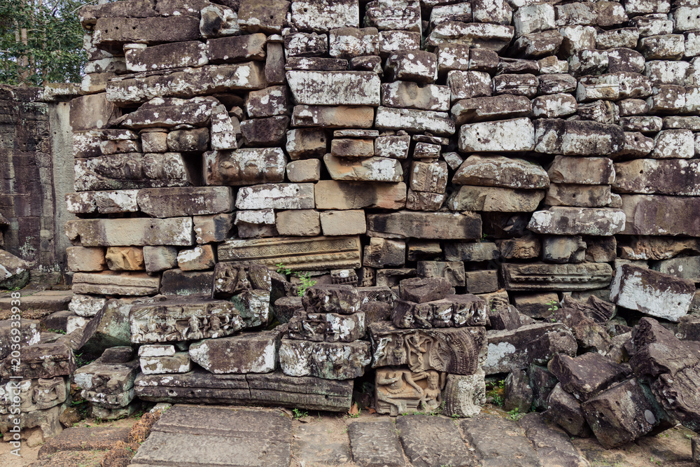 Fototapeta premium Ancient stone carvings of figures and mythical creatures adorn the weathered walls of Bayon Temple, Angkor Wat, Siem Reap, Cambodia, showcasing intricate Khmer artistry.