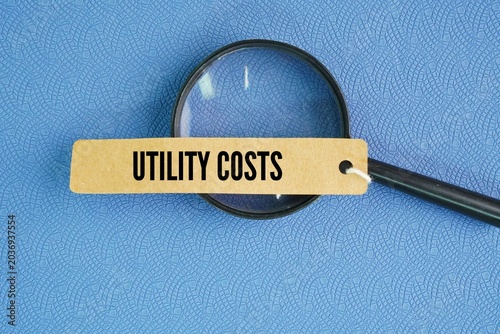 Magnifying glass and paper tag with the word utility costs. monthly or yearly expenses required to operate and maintain a home or business, primarily covering essential services like electricity
