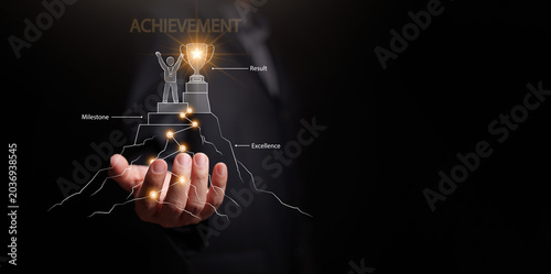 Businessman hand with glowing achievement path to trophy on mountain peak on dark copy space. Personal development, milestone, excellence, self improvement, educational growth, goal accomplishment.