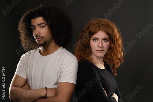 Young mixed race couple standing back to back with crossed arms, expressing tension and misunderstanding