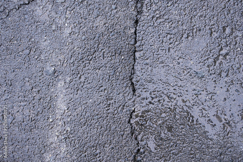 Detailed texture of damp dark asphalt with a deep vertical crack, industrial nature background