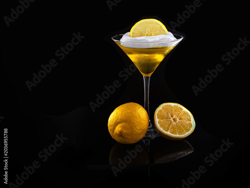 A vibrant lemon desert topped with cream and a lemon slice, photographed in an elegant martini glass on a glossy black background—fresh citrus mood and sophisticated beverage styling for food and drin