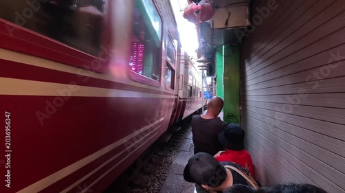 Tourists standing extremely close to the wall as a red train passes through the famous Hanoi Train Street in Vietnam.