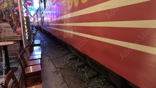 A red and white train passing closely through the famous Hanoi Train Street cafe in Vietnam.