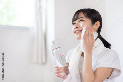 Bilde på lerret Young Asian woman smiling while wiping sweat with towel in bright room