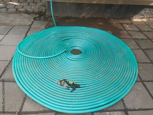 Foto High angle view of a green rubber water hose rolled on paved ground
