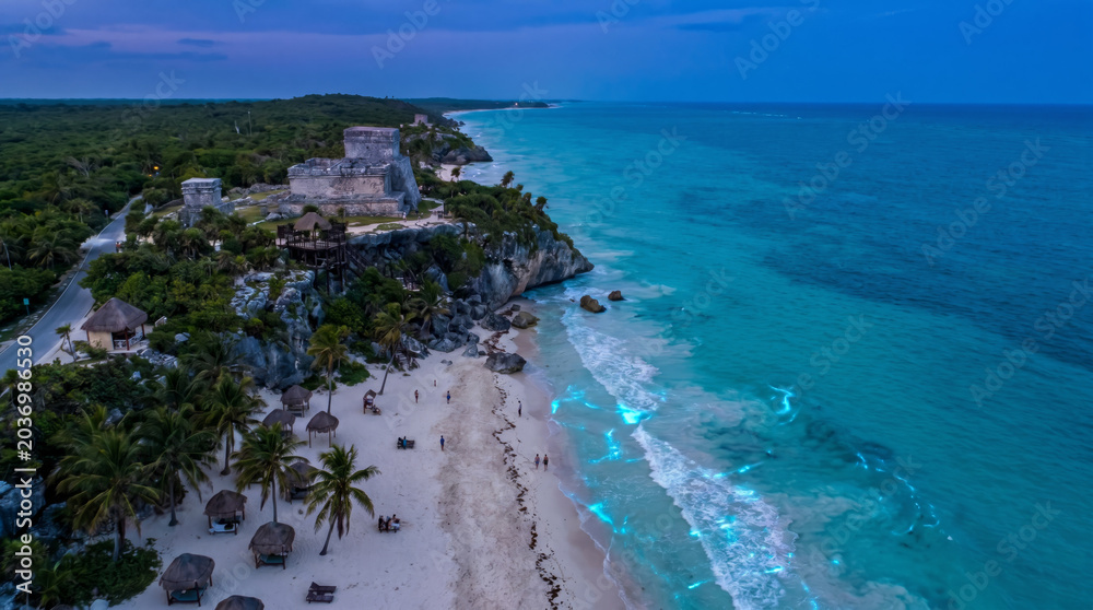 Fototapeta premium Majestic Mayan ruins of Tulum perched on a cliff overlooking the turquoise Caribbean Sea at sunset.