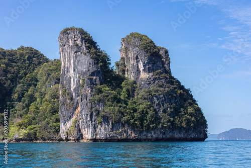 Towering limestone cliffs at Railay Beach in Krabi, southern Thailand. Bay in the foreground; blue sky overhead.
