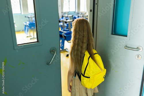 Young girl entering an empty classroom with a yellow backpack