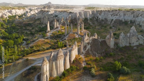 Goreme, Nevsehir, Turkey. Love Valley fairy chimneys, tall volcanic tuff pillars with dark basalt capstones, aerial view at golden hour over the eroded Cappadocian landscape. Aerial View