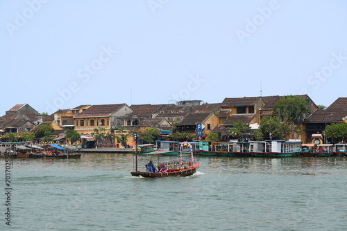 Photos A wooden boat navigates the calm river waters with the historic yellow architect