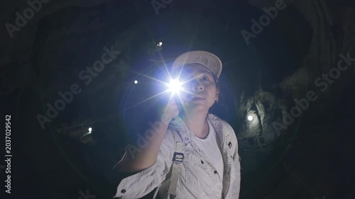 Asian woman adventurer exploring a dark underground cave with a flashlight.