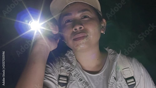 Asian woman adventurer exploring a dark underground cave with a flashlight.
