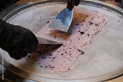 Close up of street vendor hands using metal spatulas to chop and mix ingredients for stir-fried ice cream roll on a freezing cold steel plate at a night market stall.