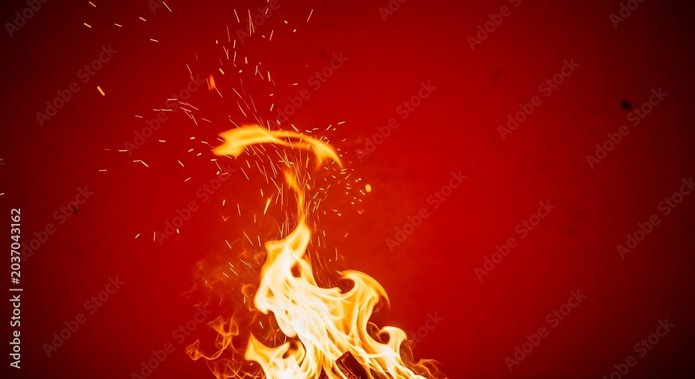 Fototapeta premium Bright orange fire flames with flying sparks over red background