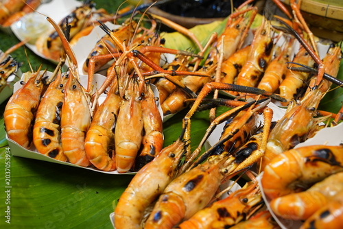 Delicious grilled giant river prawns arranged on a tray lined with traditional green banana leaf at an Asian street food market.