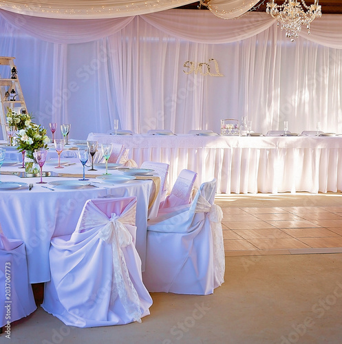 Luxurious wedding reception venue with white drapery, crystal chandeliers, and elegantly styled dining tables prepared for celebration.