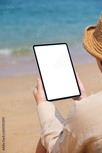 Vertical mockup image of a woman holding a digital tablet with blank desktop screen by the sea