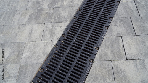 Billede på lærred A metal drainage grate is installed on grey paving slabs in the city centre