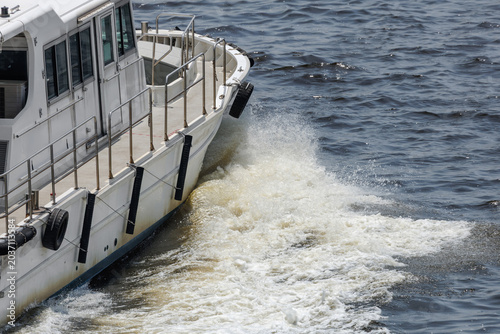 Photos Small utility workboat with black fenders cuts through murky waters of a choppy harbor, churning out a tea-colored wake along its starboard side as sunlight glints off foamy spray