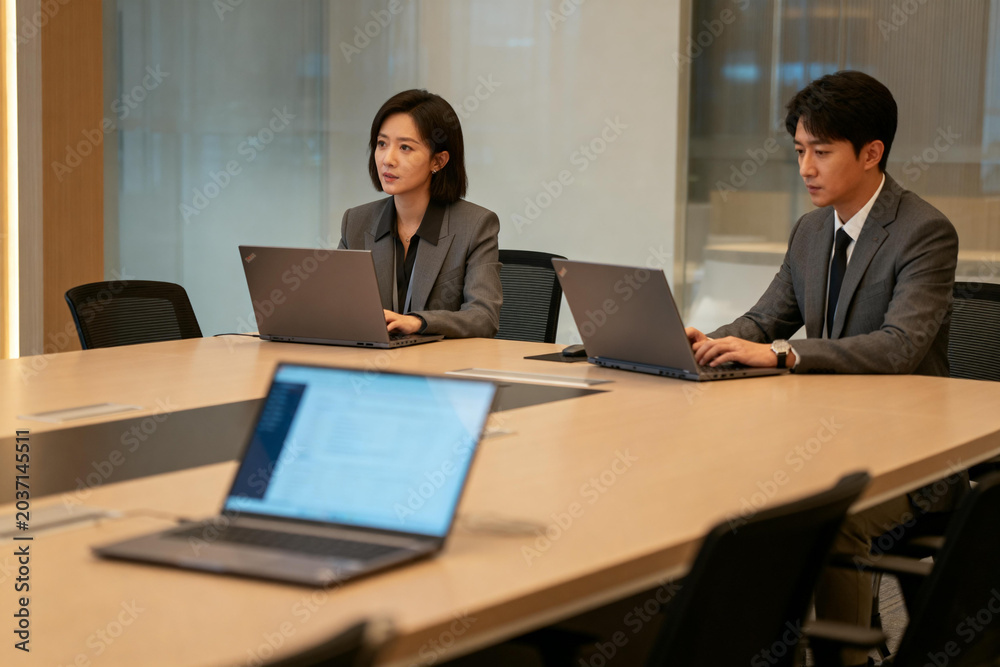 Fototapeta premium Two business professionals working on laptops in a modern conference room