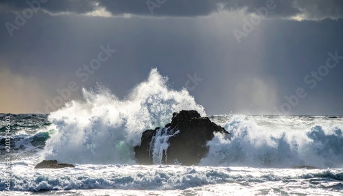 Powerful ocean wave powerfully crashes over a submerged dark rock, sending sea foam exploding outwards in a dynamic display of nature's force