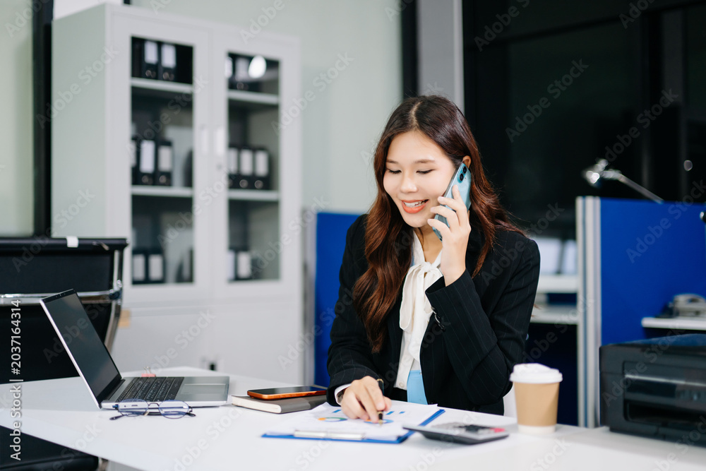 Fototapeta premium Professional Asian businesswoman talking on smartphone while working in modern office, corporate communication and productivity concept.