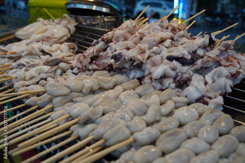 A large display of uncooked squids, including tentacles and white eggs on bamboo skewers, stacked nicely at an Asian night market stall.