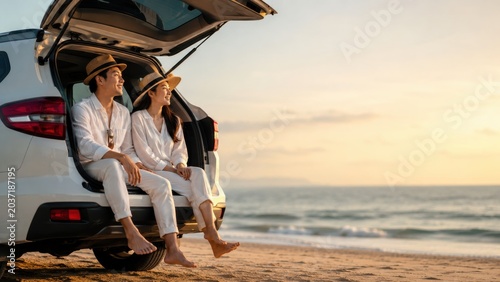 Couple relaxing in car trunk watching sunset on beach during road trip adventure.