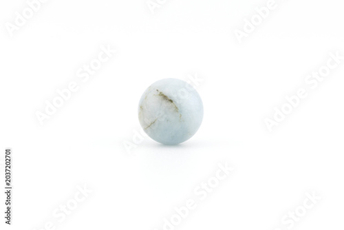 An aquamarine stone rests on a white surface. The stone has smooth edges and a light blue color with subtle veins running through it. The light creates reflections.