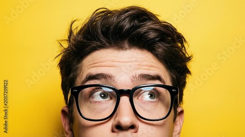 Young man with glasses looking up curiously against a bright yellow background