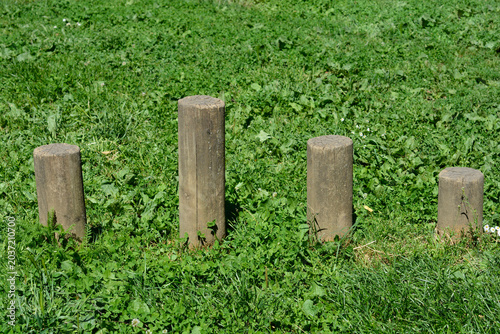 Four vertical wooden stepping posts of different heights installed in a row on green grass at a children playground.