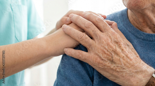 Elderly man receiving care with nurse's hand on shoulder indoors  