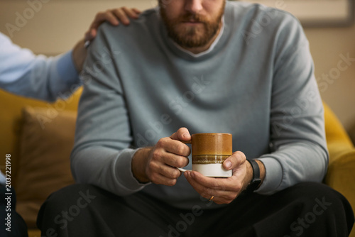 Quadro su tela Caucasian young adult men sitting together, offering shoulder support and holding mug, expressing male friendship and emotional care